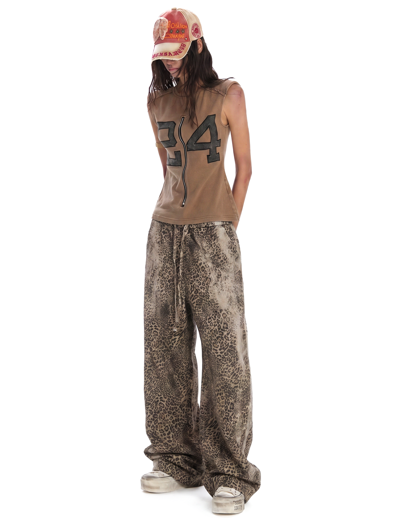 Three-quarter view of a model in a brown "24" graphic sleeveless top and oversized leopard print wide-leg pants.