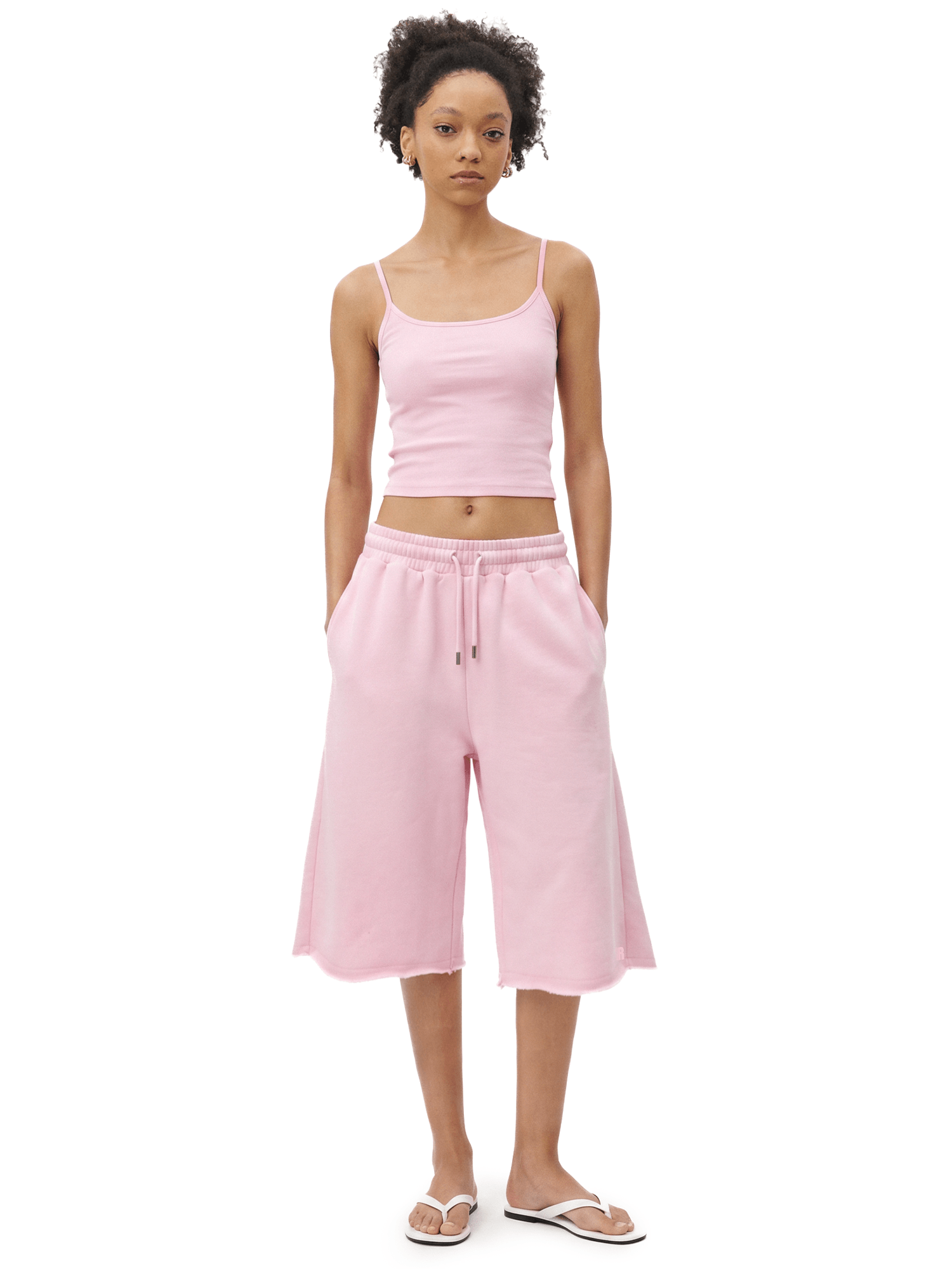 Full-body front view of a model wearing a light pink spaghetti-strap camisole cropped top and matching light pink loose knee-length shorts.