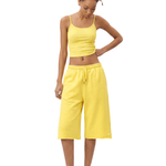 Full-body front view of a female model wearing a bright yellow spaghetti-strap camisole cropped top and matching bright yellow knee-length loose shorts, looking down with one hand on her hip.