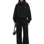 Person wearing a black tracksuit holding a black bag on a white background