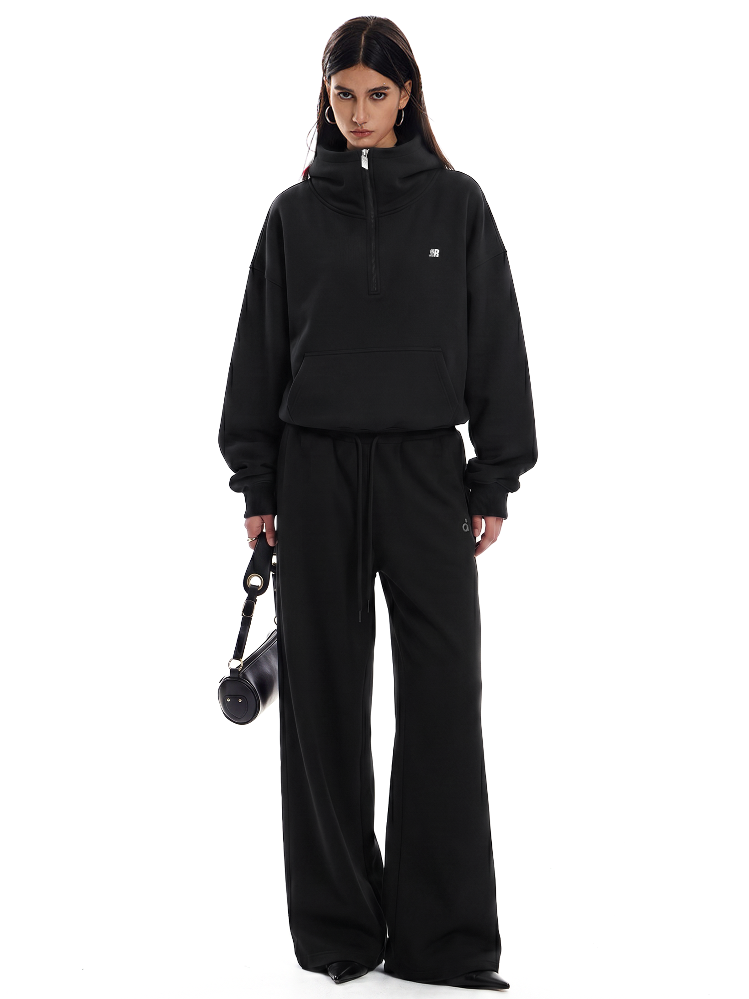 Person wearing a black tracksuit holding a black bag on a white background