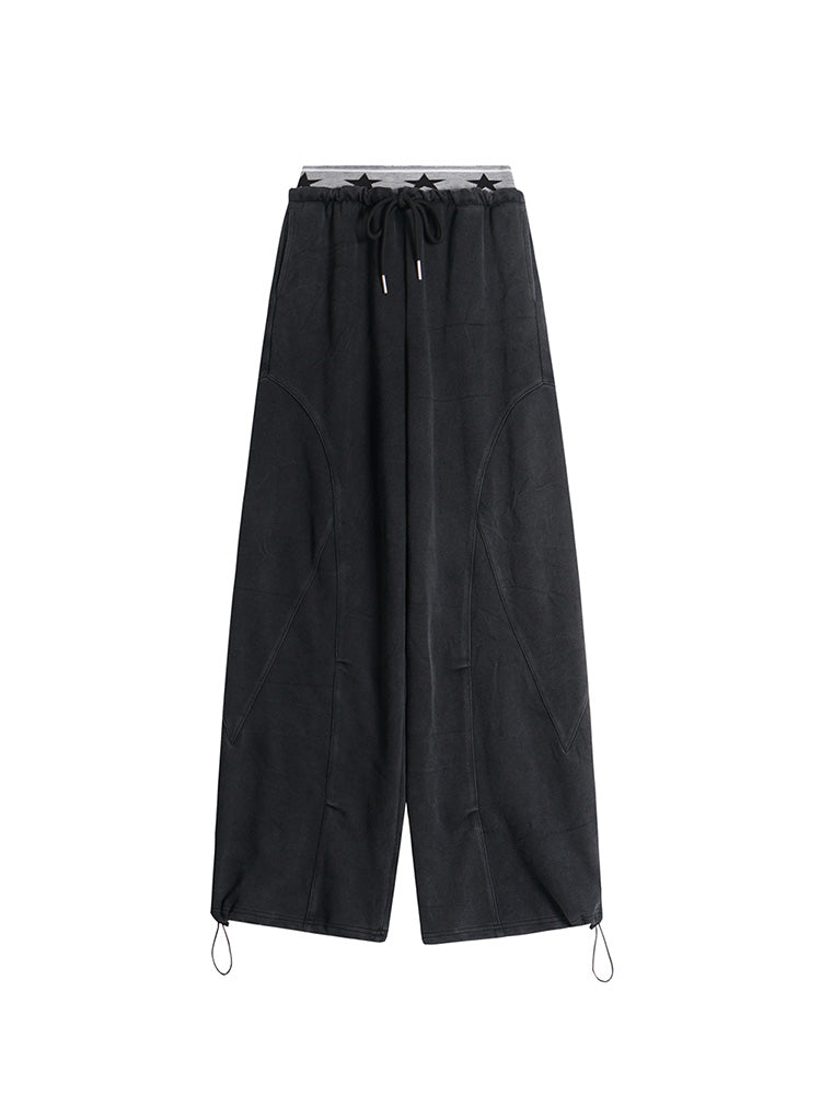 Flat lay of black high-waisted wide-leg trousers with an elastic waistband and toggle hem details.