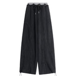 Flat lay of black high-waisted wide-leg trousers with an elastic waistband and toggle hem details.