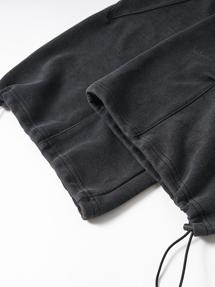 Detailed shot of the adjustable drawstring hem and toggle on black technical fabric pants.