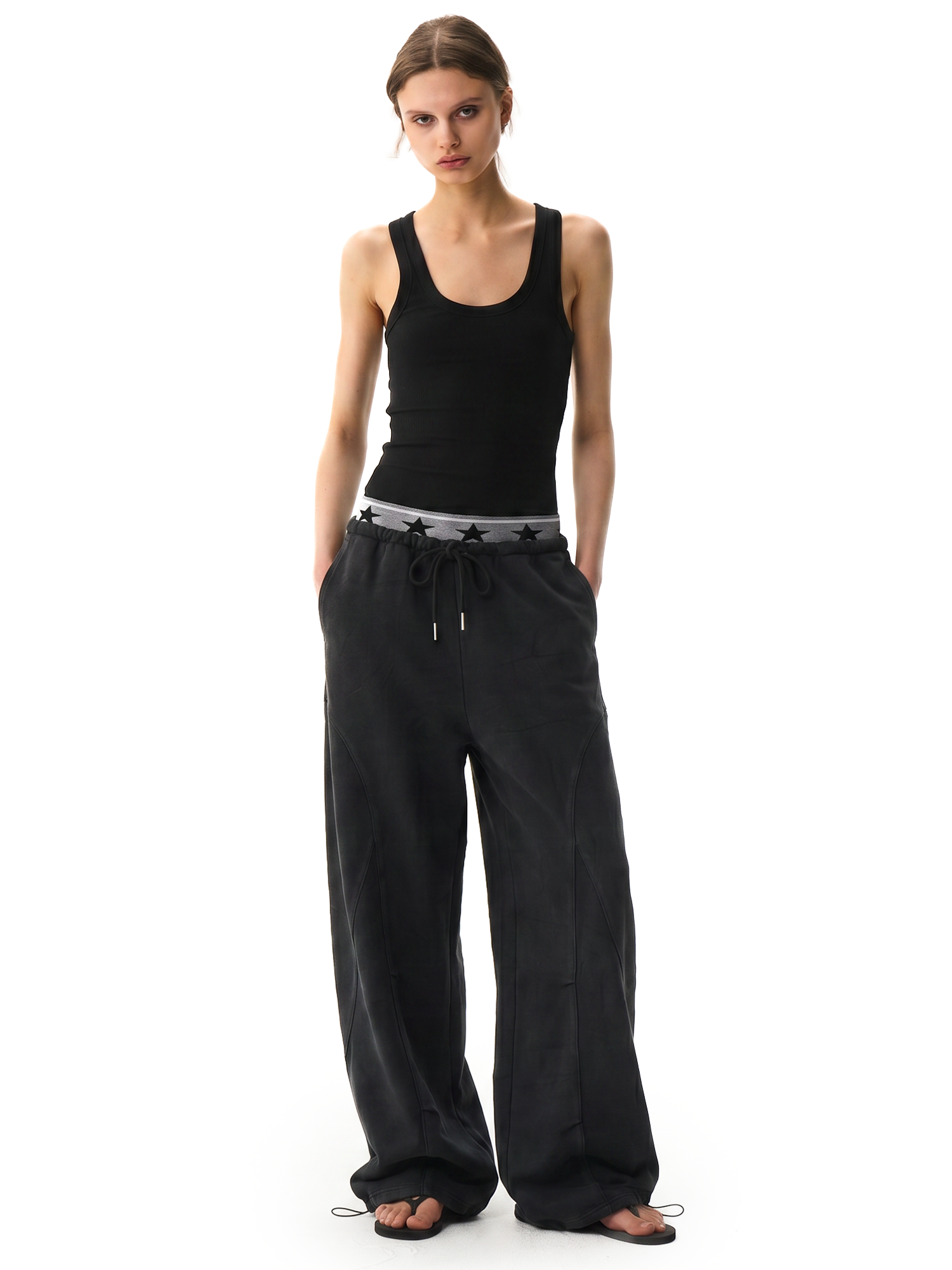 Front view of a female model wearing high-waisted black wide-leg cargo pants and a black ribbed tank top.