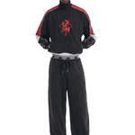 Front view of a male model wearing black wide-leg drawstring sweatpants and a black zip-up track jacket with red stripes.