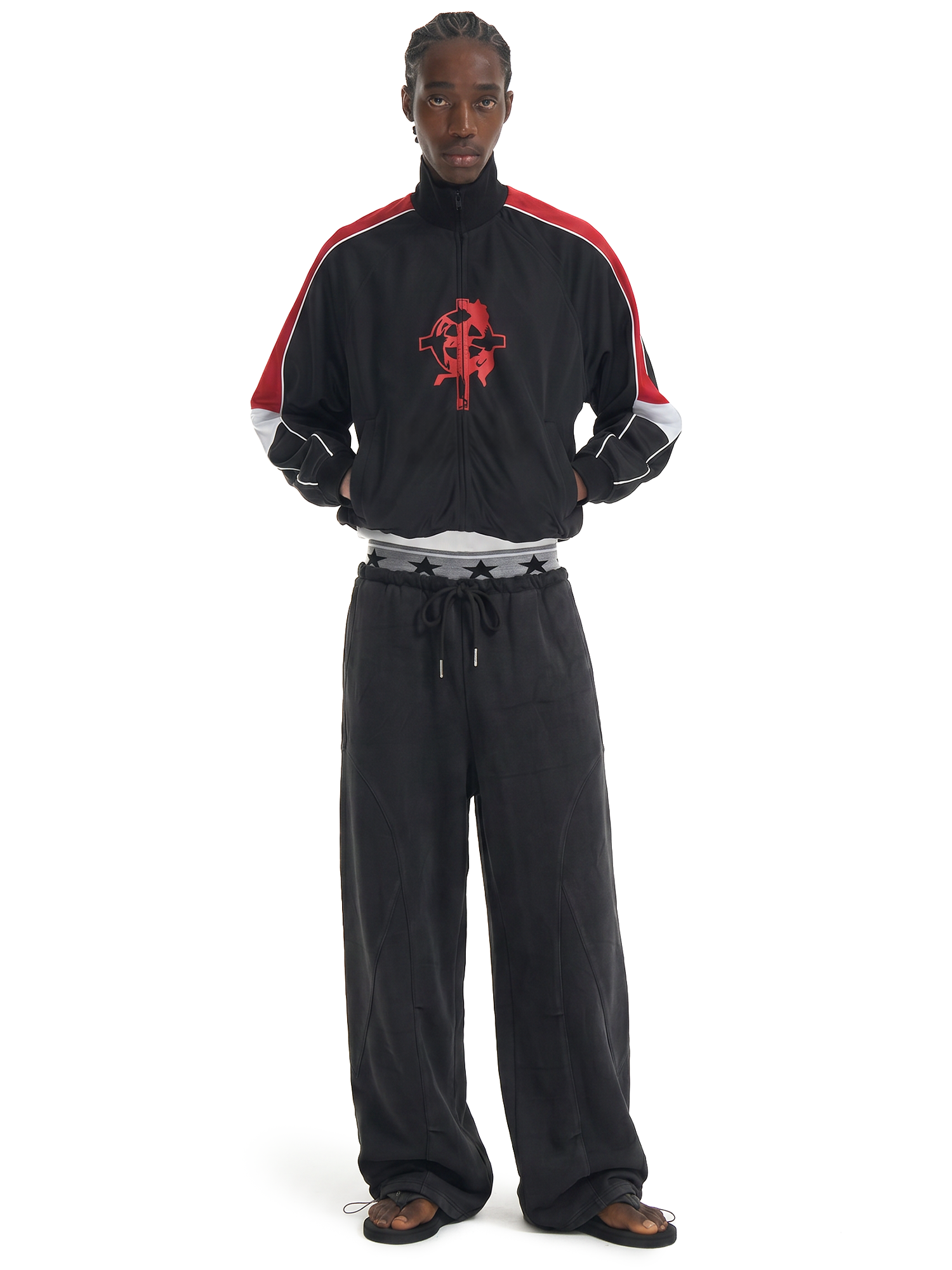Front view of a male model wearing black wide-leg drawstring sweatpants and a black zip-up track jacket with red stripes.