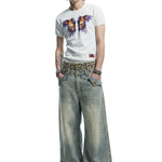 Front view of a male model wearing a white graphic butterfly t-shirt and light wash oversized baggy denim jeans with a leopard print waistband.