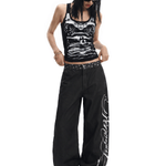 Full-body view of a model wearing the black graphic tank top paired with long, loose black wide-leg trousers and dark shoes.