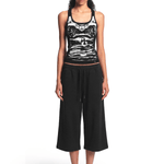 Full-body straight-on front view of a model wearing the black graphic tank top and black cropped pants with sandals.