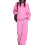 Model wearing pink oversized hoodie and sweatpants set with a baseball cap and backpack, full body view