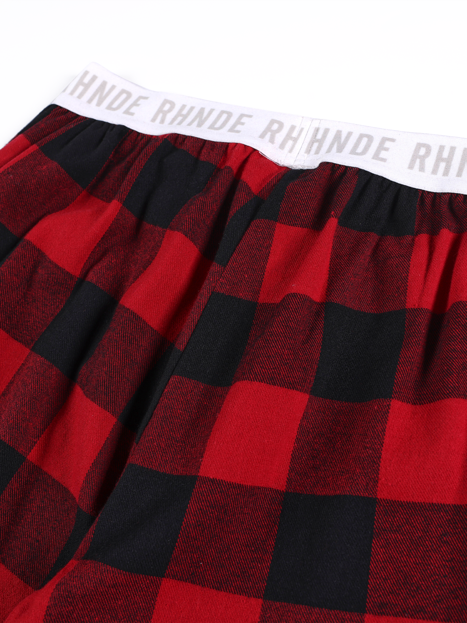 Close-up of white elastic waistband with bold black typography on plaid baggy pants.