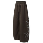 Side profile of baggy dark brown sweatpants showing loose fit and graphic detail.