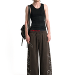 Male model wearing oversized dark brown wide-leg sweatpants with white graphic print and black tank top, street style fashion.