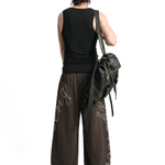 Back view of male model in baggy dark brown joggers featuring leg graphics and a black backpack.