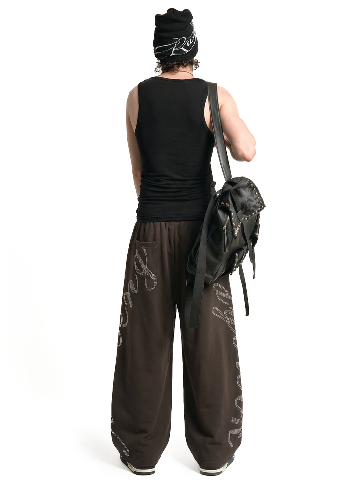 Back view of male model in baggy dark brown joggers featuring leg graphics and a black backpack.