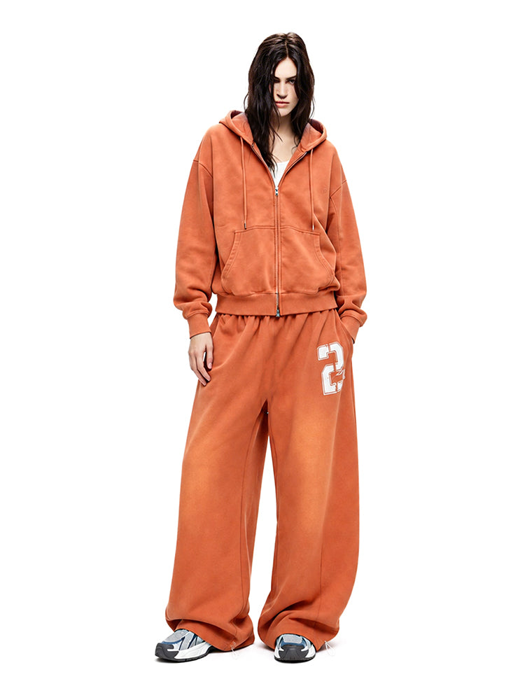 Full-body shot of a model wearing a vibrant orange hoodie and matching wide-leg track pants.