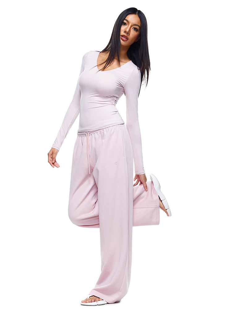 Full-body shot of a model wearing soft pink wide-leg sweatpants and matching long-sleeve top, demonstrating a feminine and stylish interpretation of women's comfortable loungewear.