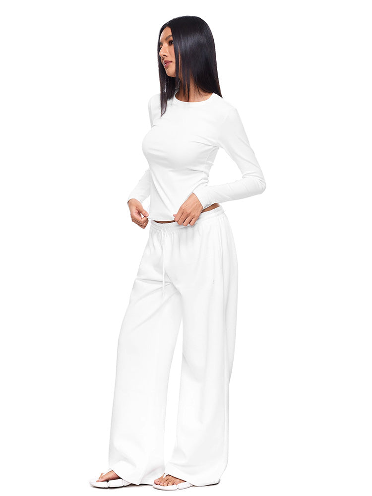 Full-body shot of a model wearing crisp white wide-leg sweatpants and matching long-sleeve top, illustrating a clean, minimal loungewear set with a relaxed, premium feel.