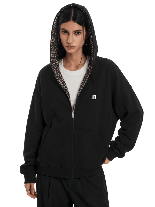 Personne portant un sweat à capuche noir avec une doublure à imprimé léopard sur fond blanc