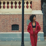 Lifestyle video of a model wearing red oversized zip-up hoodie and matching sweatpants, walking outdoors by a lake with a coffee cup, showcasing a casual streetwear style.