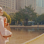Atmospheric video showcasing a trendy pink Y2K style tracksuit for women, featuring a model with a white headband and glasses in a sunny urban park setting.