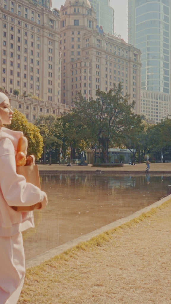 Atmospheric video showcasing a trendy pink Y2K style tracksuit for women, featuring a model with a white headband and glasses in a sunny urban park setting.